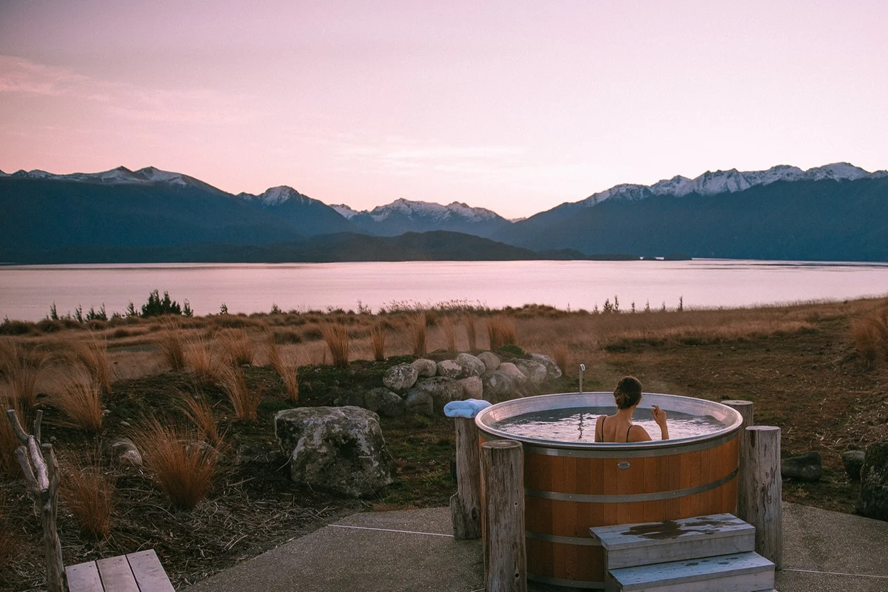 Fiordland Lodge — A guest in Fiordland Lodge's outdoor hot tub with Lake Te Anau and mountain views at dusk
