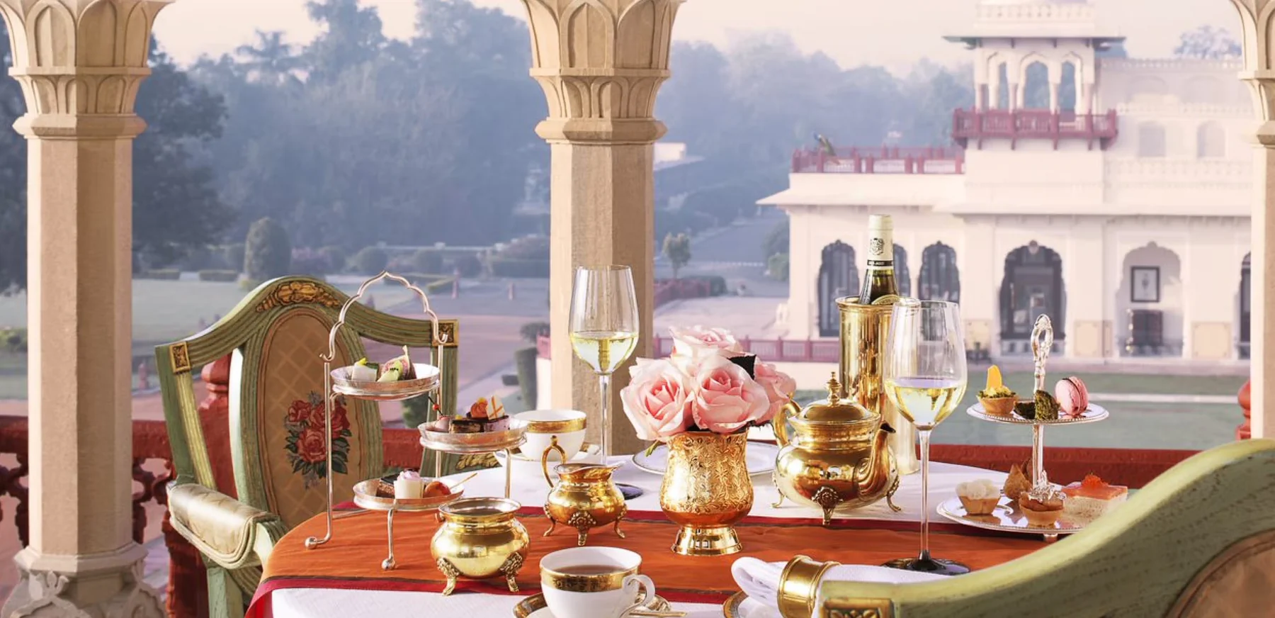 Rambagh Palace — A beautifully set dining table on Rambagh Palace's balcony with the palace gardens beyond